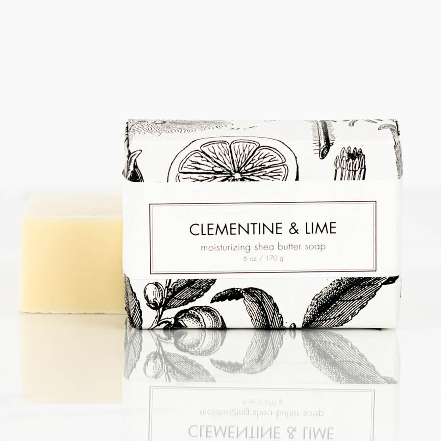 A package of Formulary55 Clementine and Lime Natural Shea Butter Bar Soap is placed next to an unwrapped bar of the same soap. The packaging features a white background with black botanical illustrations and text detailing the soap's refreshing scent and moisturizing properties.