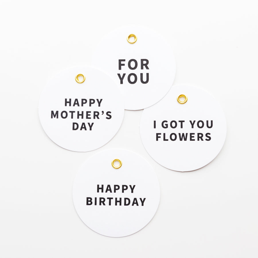 Four round white gift tags with black text and gold grommets are displayed against a white background. The tags read: "HAPPY MOTHER'S DAY," "FOR YOU," "I GOT YOU FLOWERS," and "HAPPY BIRTHDAY.