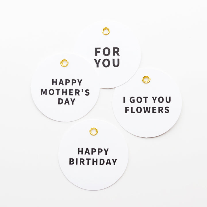 Four round white gift tags with black text and gold grommets are displayed against a white background. The tags read: "HAPPY MOTHER'S DAY," "FOR YOU," "I GOT YOU FLOWERS," and "HAPPY BIRTHDAY.