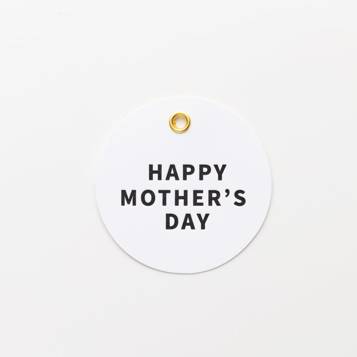 A round white tag with a small gold hole at the top center features the text "HAPPY MOTHER'S DAY" in bold, black letters in the middle. The background is plain white.