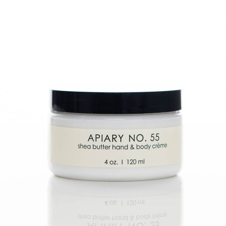 A small, round white jar with a black lid, labeled "APIARY NO. 55 shea butter hand & body crème." The jar contains 4 oz. or 120 ml of product. The label is positioned in the center with a minimalist design.