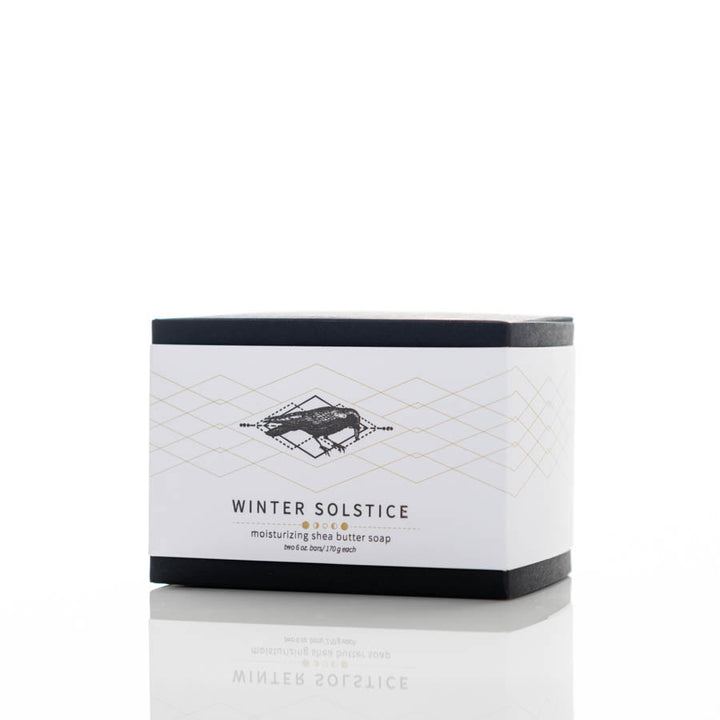 A rectangular bar of Winter Solstice moisturizing shea butter soap in a white and black box. The packaging features a geometric gold and black design with the product name and description in black text. The box is positioned against a white background.