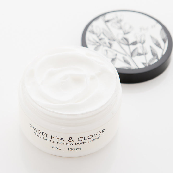 A jar of "SWEET PEA & CLOVER" shea butter hand & body crème is open, revealing its white creamy contents. The jar is 4 oz (120 ml), and the lid with a botanical black and white design is placed beside it.