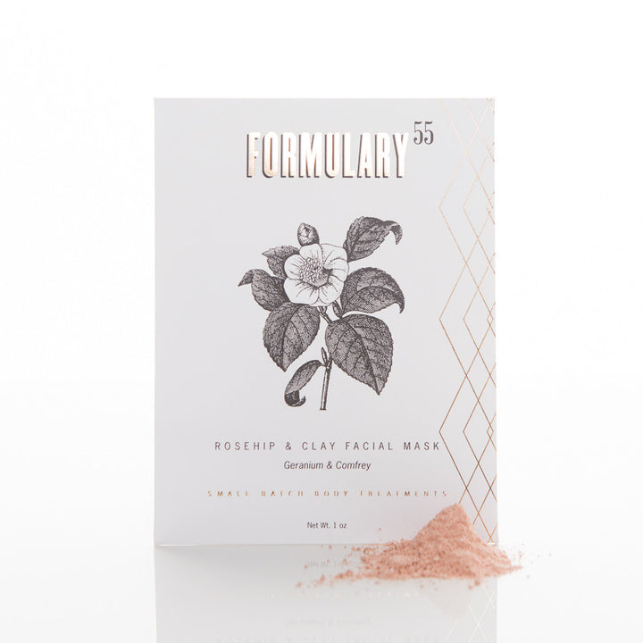 A white box with a black and white sketch of a flower and leaves on the front. The box is labeled "Formulary 55 Rosehip & Clay Facial Mask, Geranium & Comfrey." A small amount of pink powder is spilled in front of the box.