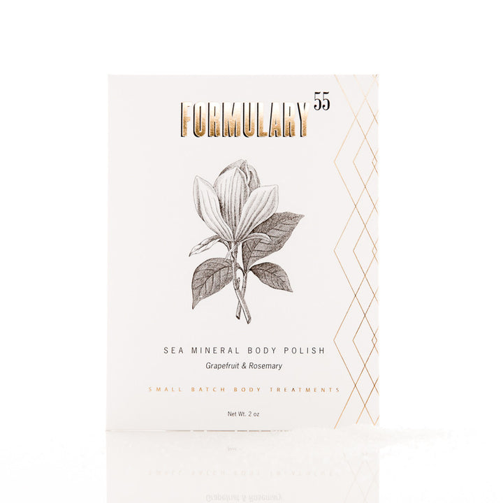 A rectangular white package of Formulary 55 Sea Mineral Body Polish in Grapefruit & Rosemary scent. The package features an illustrated magnolia flower, gold geometric lines on the right side, and gold text. It indicates "Small Batch Body Treatments" and weighs 2 oz.