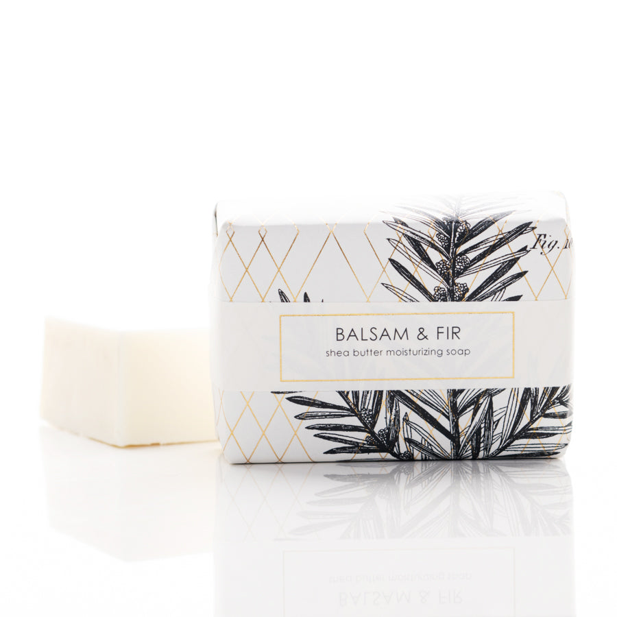 A bar of soap sits next to its partially unwrapped packaging. The packaging reads "BALSAM & FIR shea butter moisturizing soap" and features a botanical design with pine branches and a geometric gold pattern.